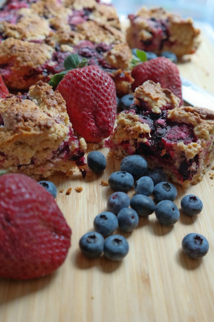 Bucati de prajitura crumble cu ovaz si fructe de padure, decorate cu capsuni si afine proaspete