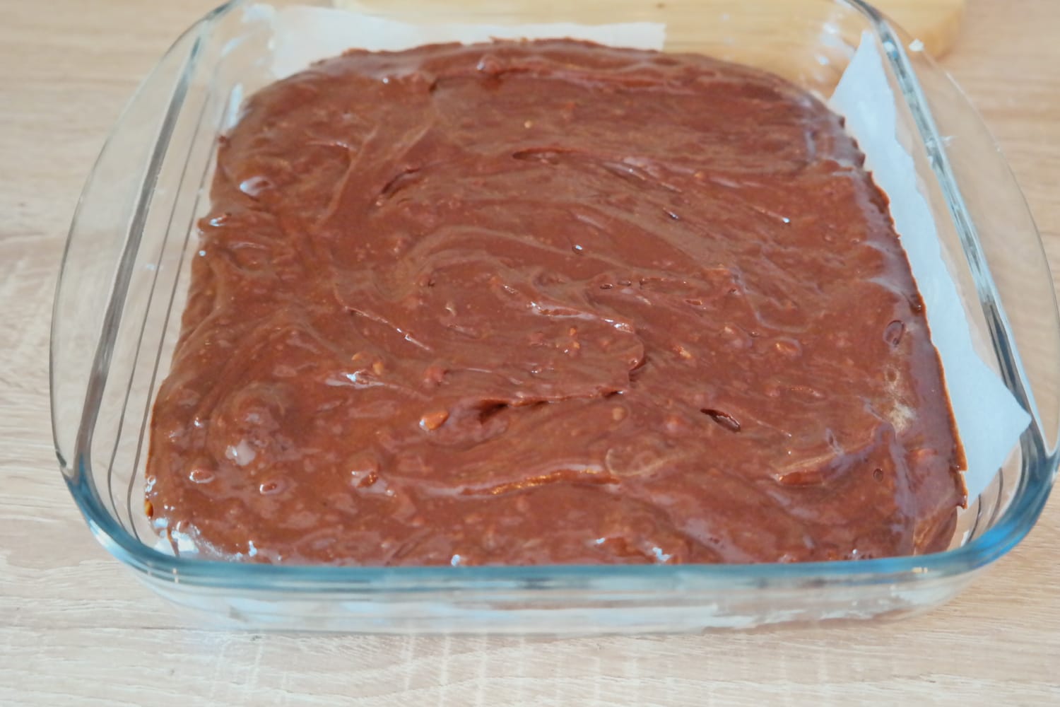 Compoziție de brownie cu nuci întinsă într-o tavă pătrată din sticlă, tapetată cu hârtie de copt