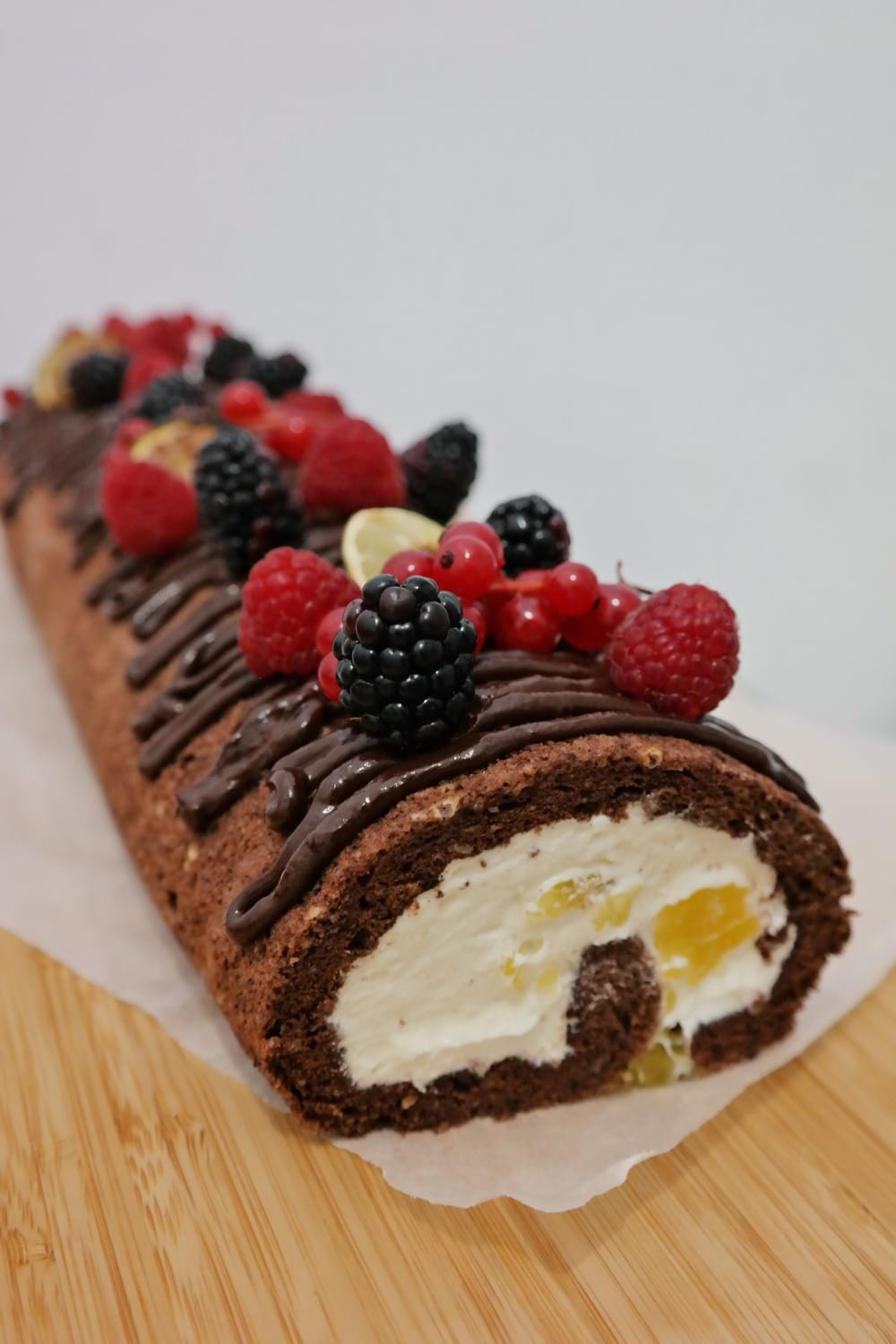Slice of cocoa roll cake with vanilla cream and pieces of orange jelly, decorated with chocolate, raspberries, blackberries, red currants and lime