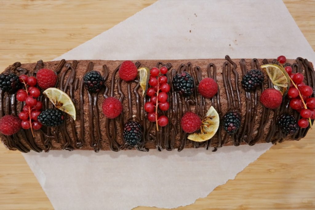 Cocoa roll cake decorated with melted chocolate, raspberries, blackberries, red currants and lime slices