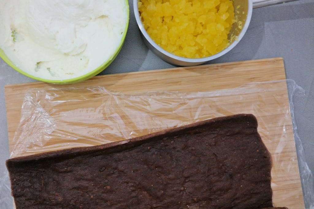 Cocoa sponge cake rolled on a cutting board, ready to be filled with vanilla cream and orange jelly