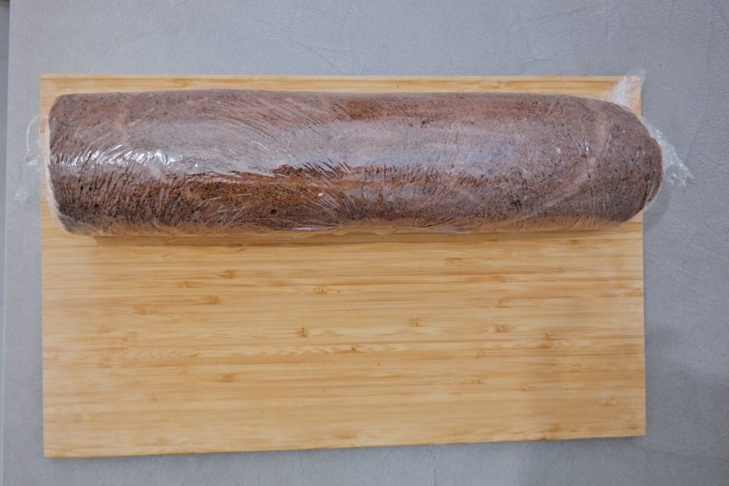 Cocoa roll cake filled with vanilla cream and orange jelly, wrapped in plastic wrap for chilling