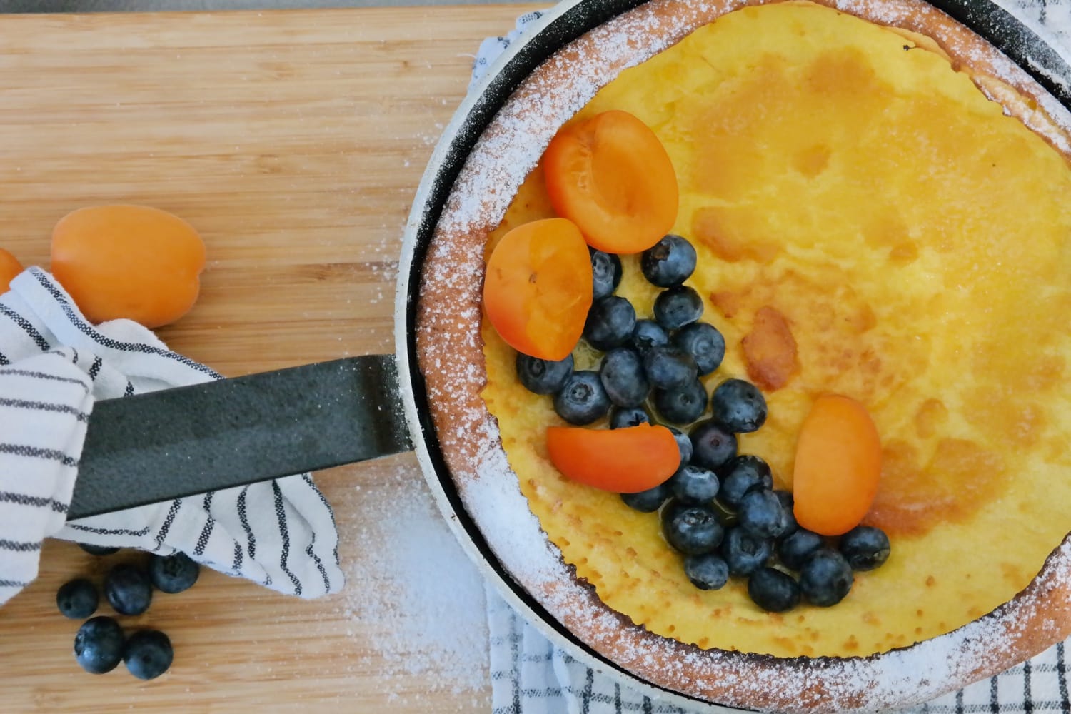 Dutch Baby Pancake served in a skillet with fresh blueberries, apricots and powdered sugar.