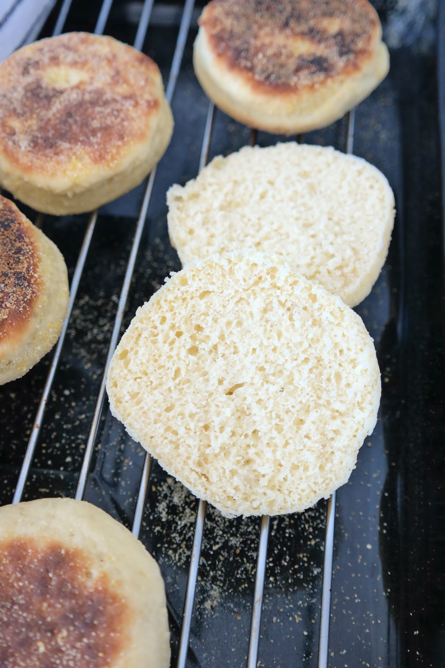 English muffin cut in half, showing its soft and airy interior, with other golden brown muffins on a cooling rack