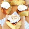 Soft cinnamon roll served on baking paper and a cloth napkin, generously topped with fluffy white cream cheese frosting and sprinkled with ground cinnamon.