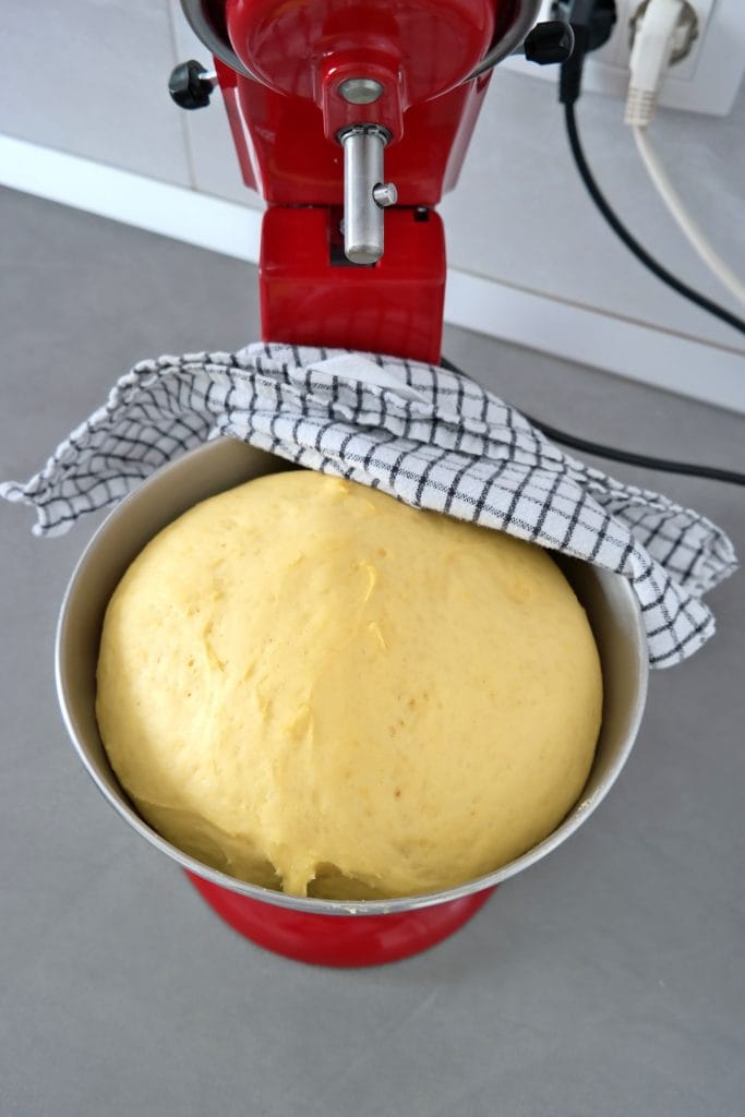 Cinnamon roll dough doubled in size after proofing inside a stand mixer bowl, covered with a kitchen towel.