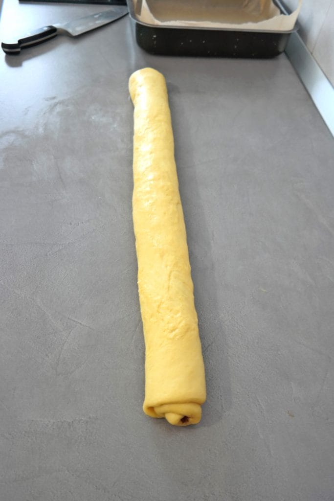 Cinnamon roll dough rolled tightly into a long log on a countertop, ready to be sliced into individual rolls.