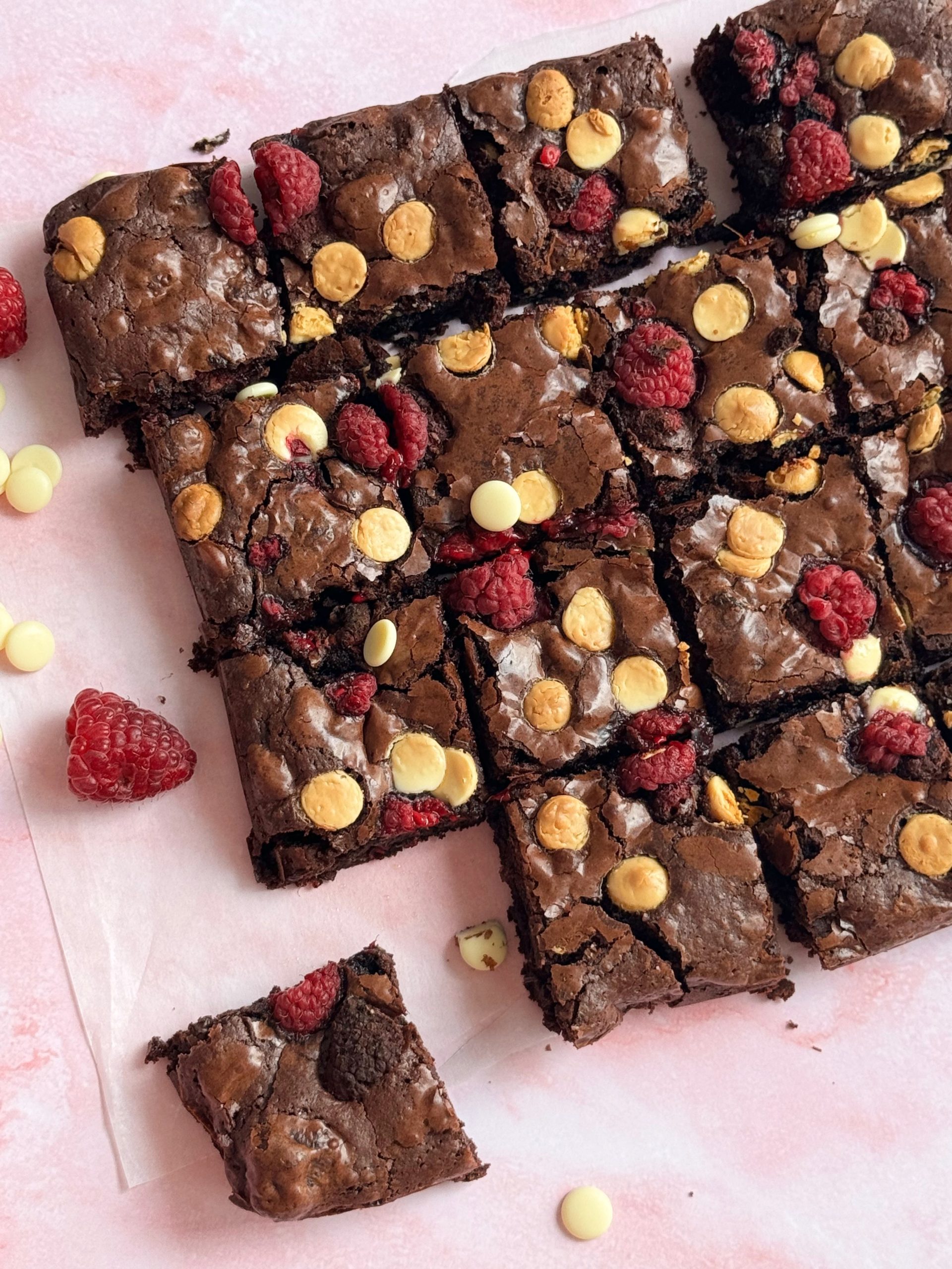 Cuburi de brownie dense si umede cu zmeura liofilizata si ciocolata alba pe hartie de copt