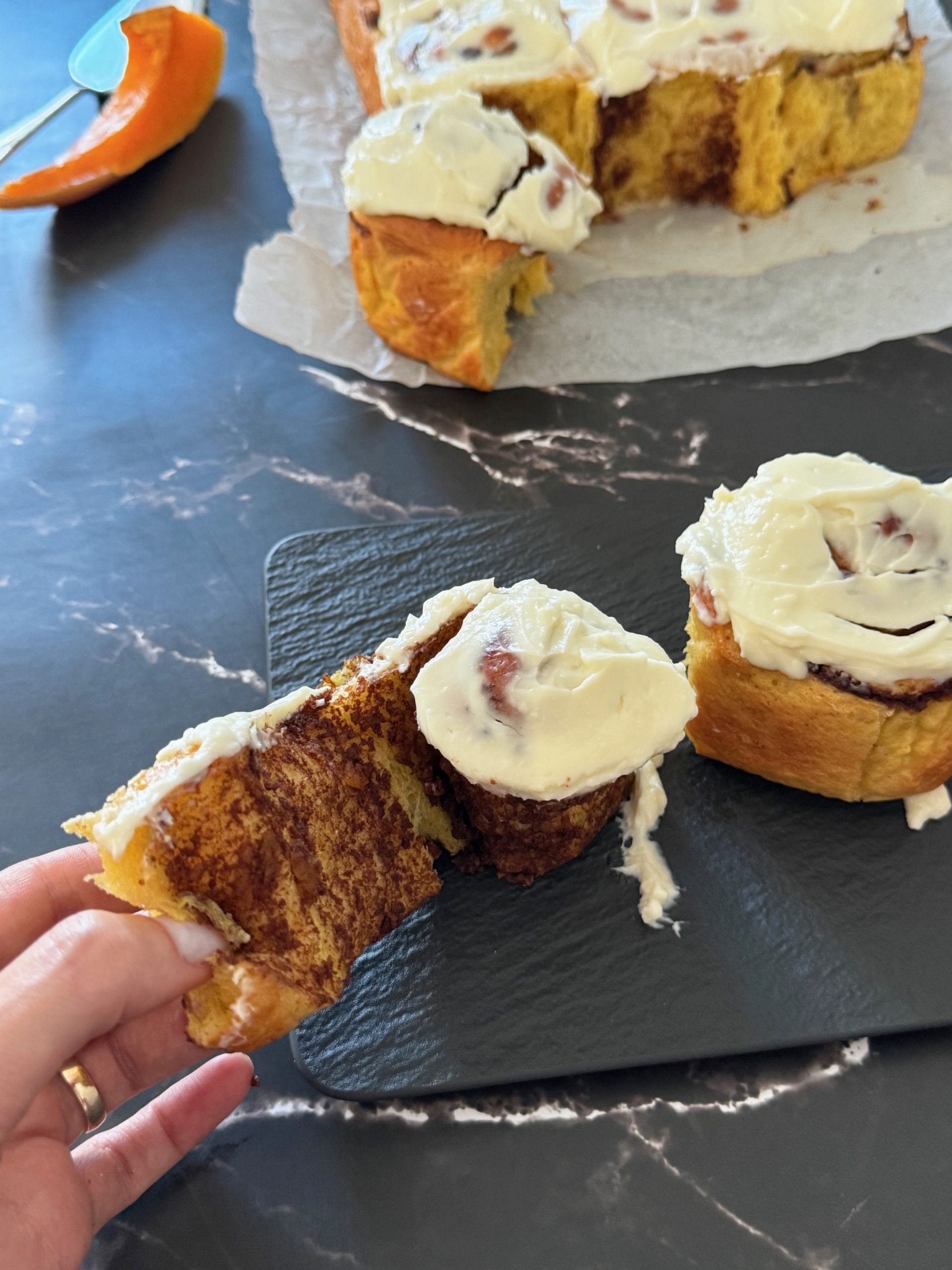 Soft pumpkin cinnamon roll with cream cheese frosting held in hand