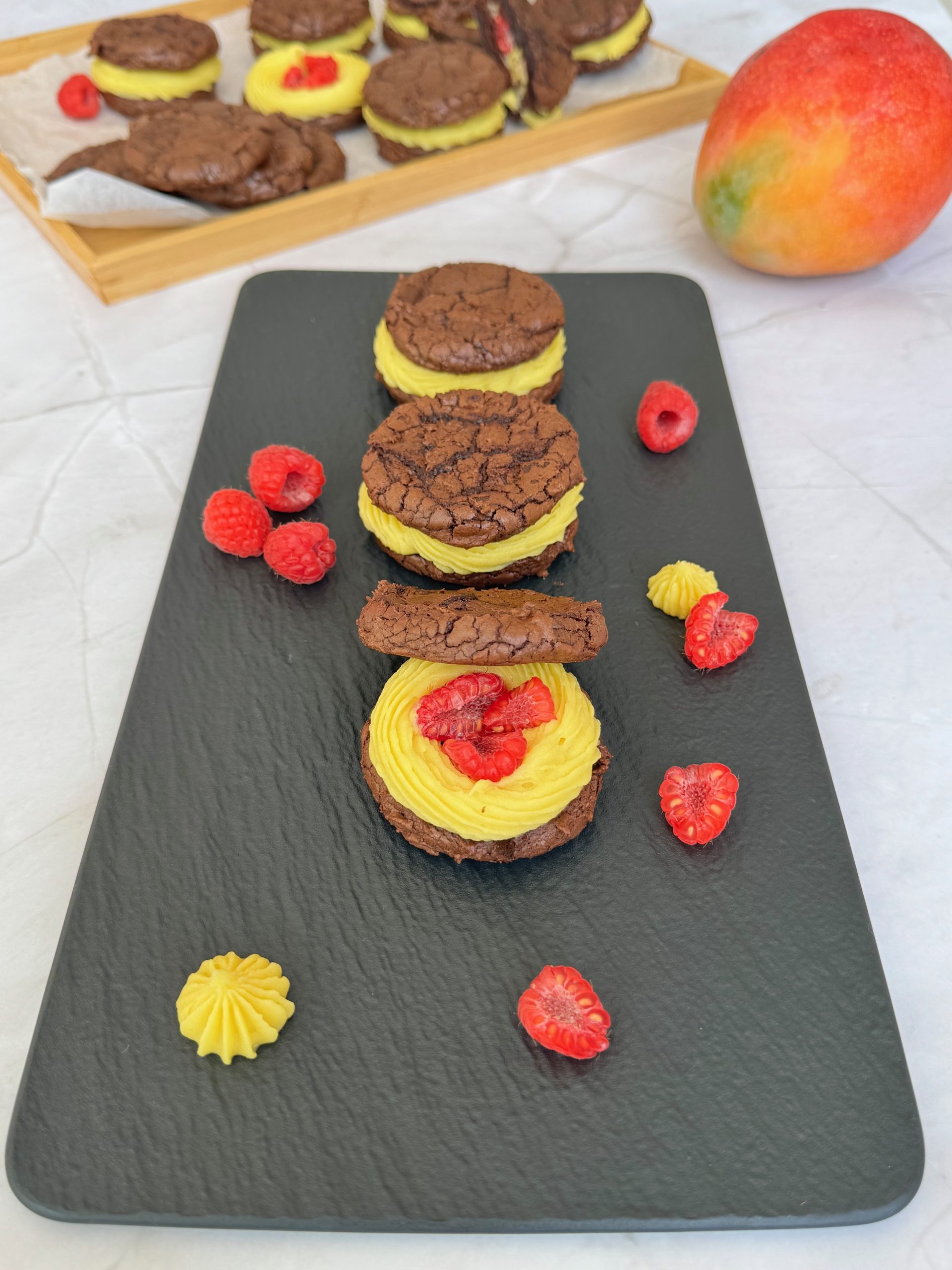 Chocolate sandwich cookies with mango and raspberry ganache