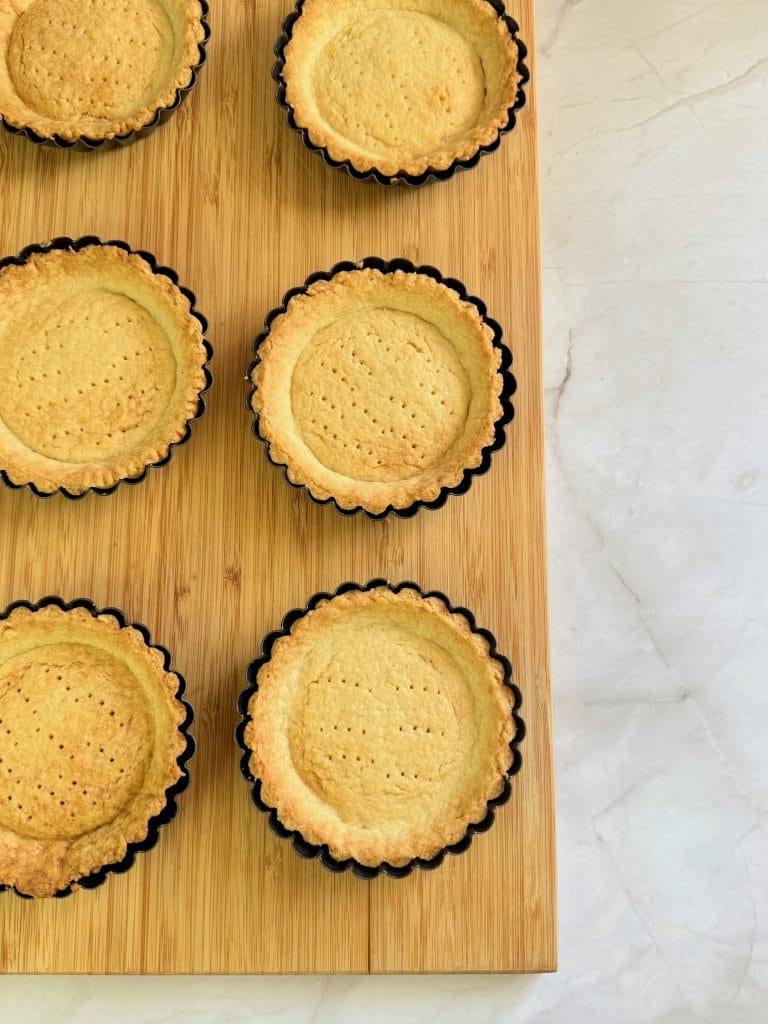 Baked golden mini tart shells cooling on a wooden board