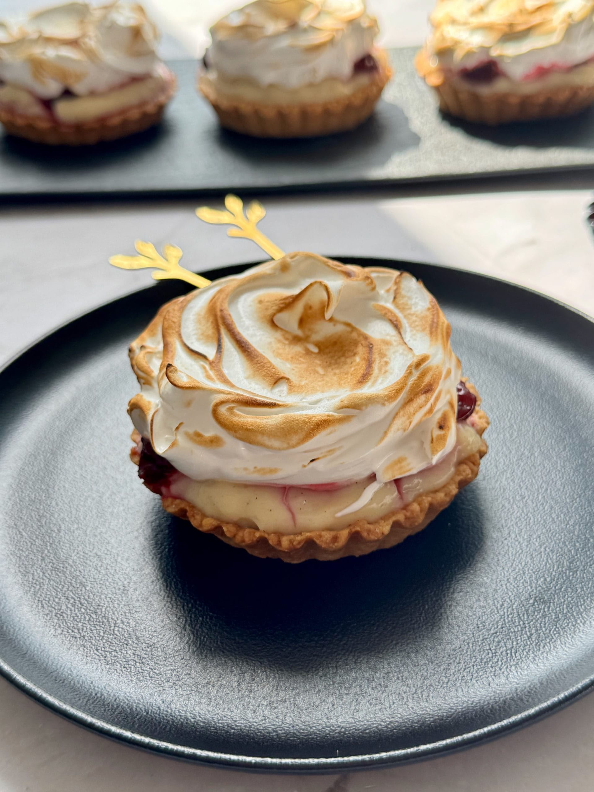 Close-up of a mini sour cherry tart with flamed meringue on a black plate