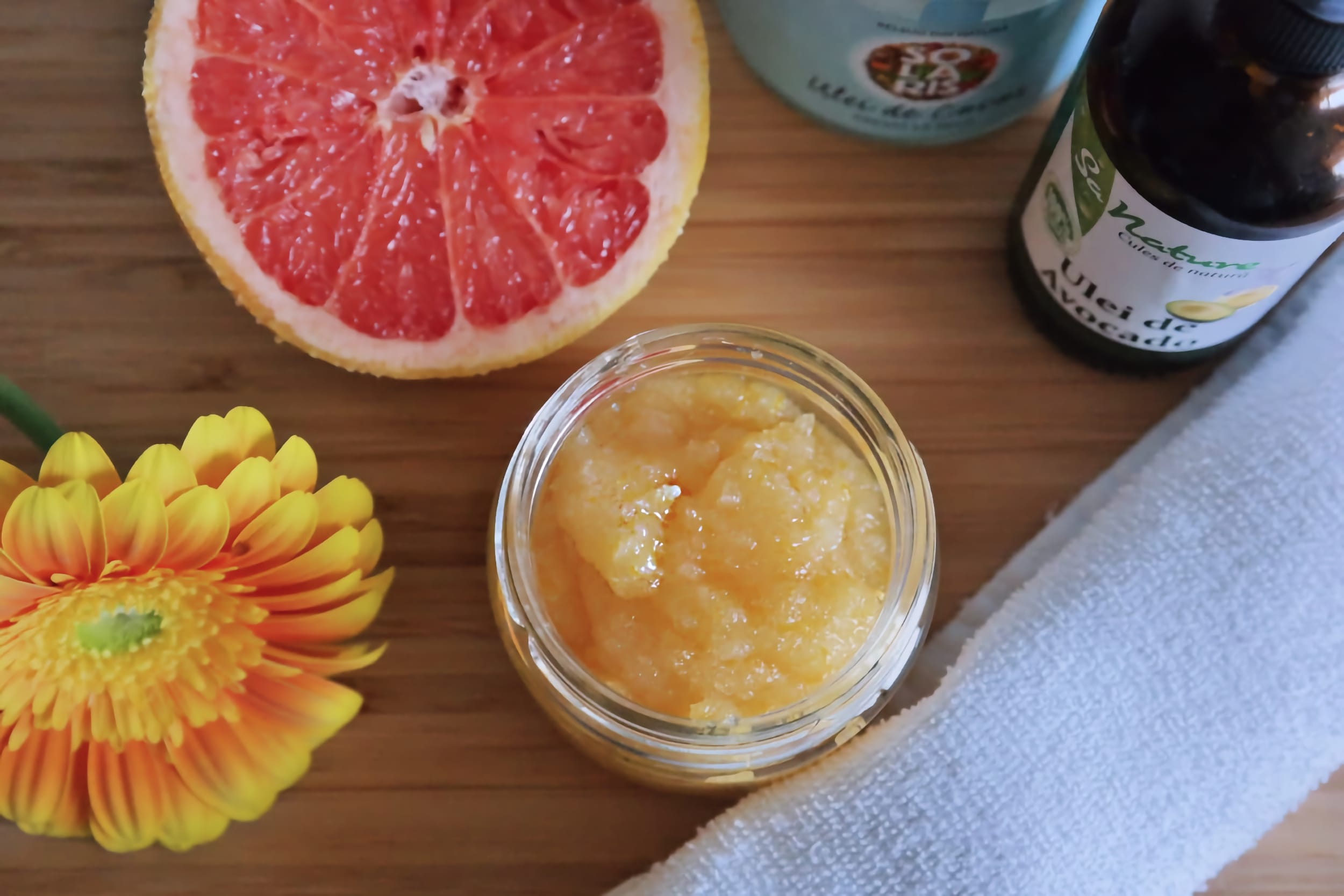 Jar of homemade grapefruit body scrub with fresh grapefruit, avocado oil and coconut oil on a wooden surface.