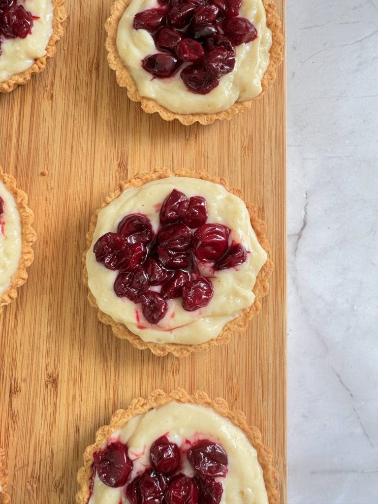 Filling mini tart shells with vanilla pastry cream and sour cherries