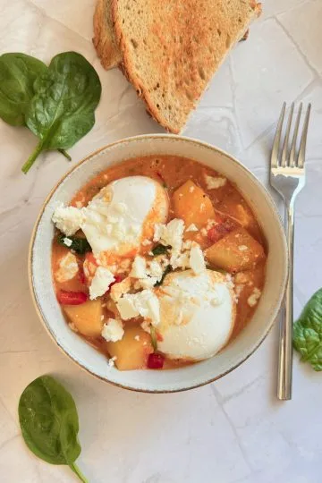 O portie de shakshuka cu cartofi si spanac, oua posate si feta servita in bol