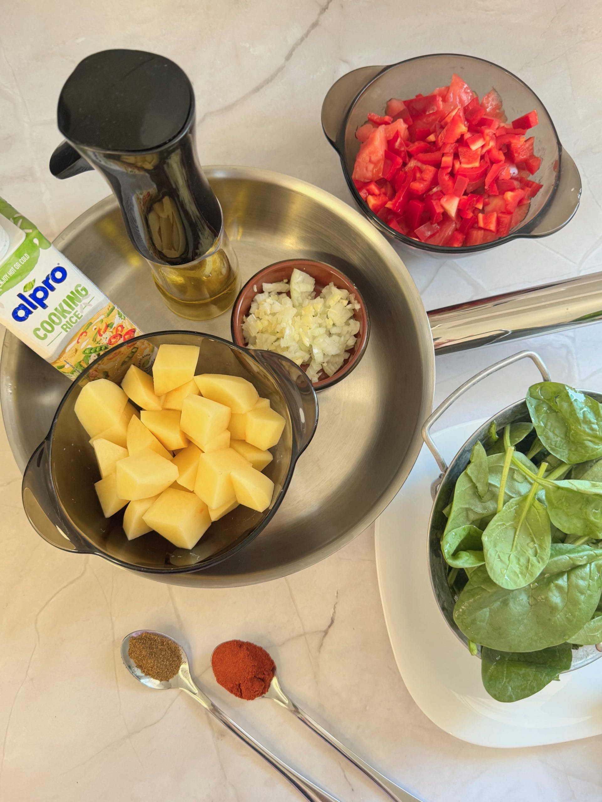 Fresh ingredients for potato and spinach shakshuka arranged on a marble surface