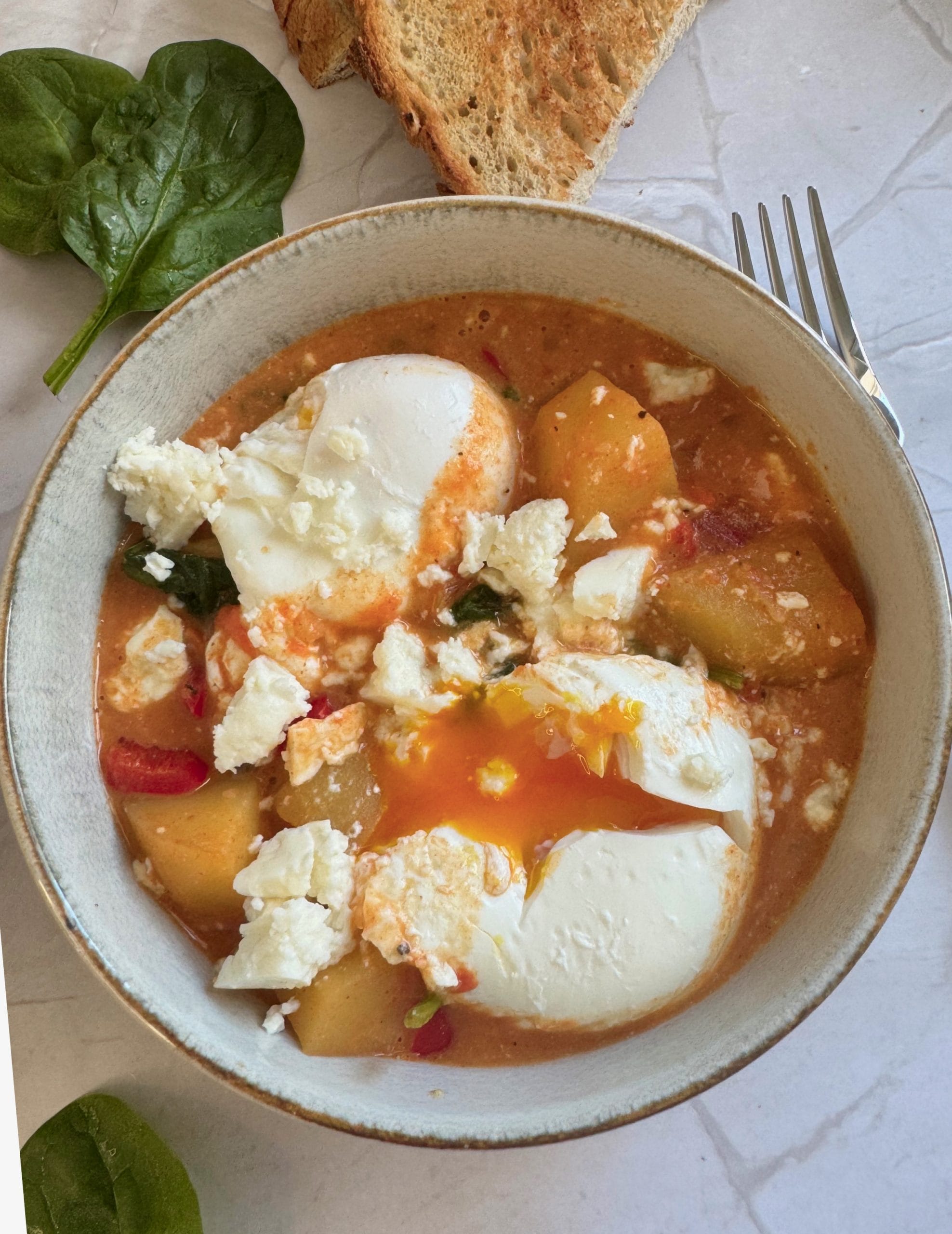 Close-up of a poached egg with runny yolk in a potato and spinach shakshuka bowl
