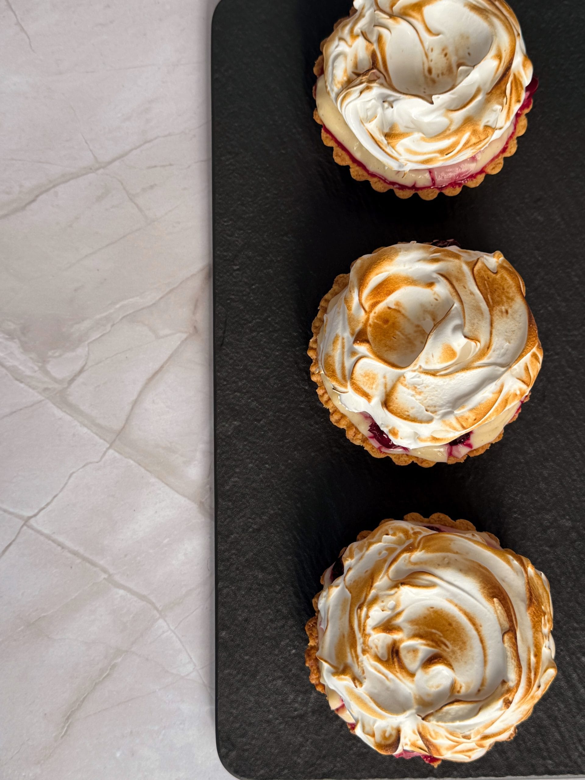 Three mini tarts with sour cherries and meringue on a black slate platter