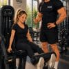 Cartoon illustration of a woman using a gym machine while being coached by a personal trainer in a modern fitness gym.