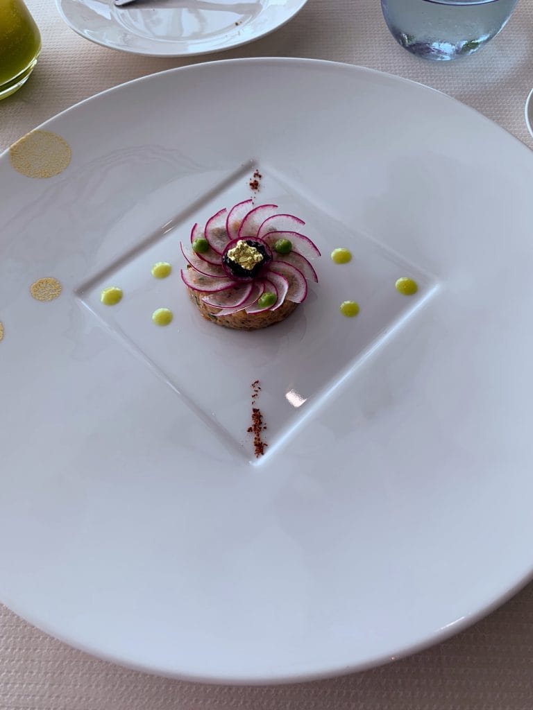Farfurie alba eleganta cu un preparat de tartar de peste decorat sub forma de floare cu felii subtiri de ridiche si foita de aur la restaurantul de lux Al Muntaha din Dubai
