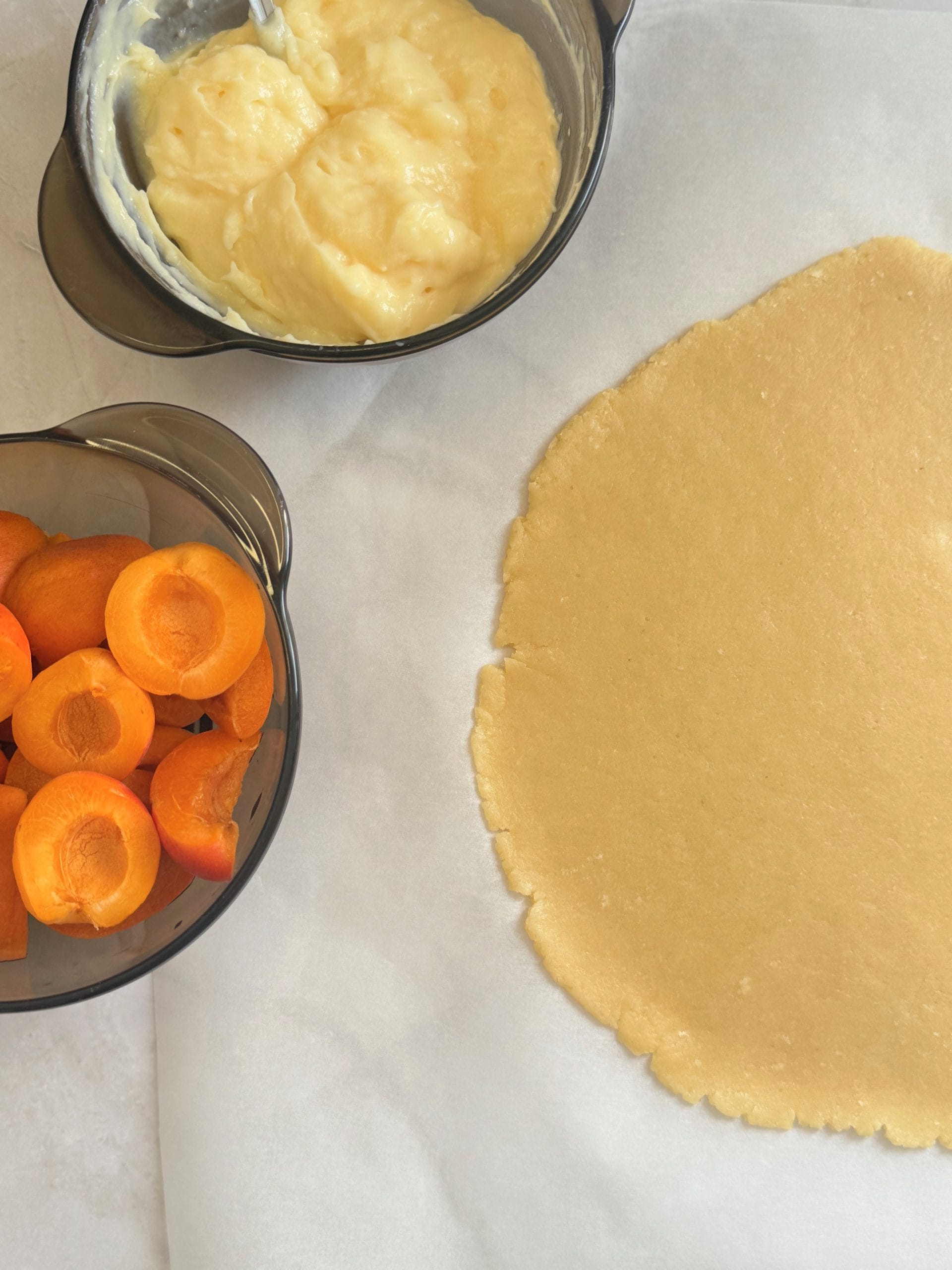 Aluat de tarta intins pe hartie de copt, crema de vanilie si caise pregatite pentru galeta
