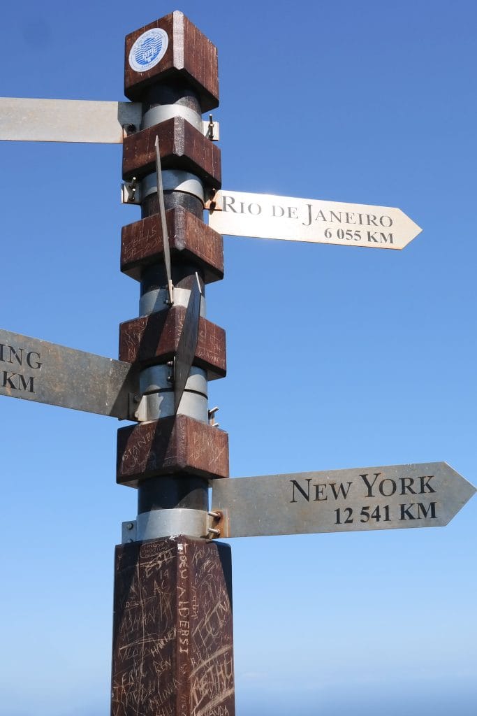 O sectiune a stalpului indicator cu sageti care indica spre Rio de Janeiro (6.055 km) si New York (12.541 km), pe fundalul cerului senin in Cape Town.