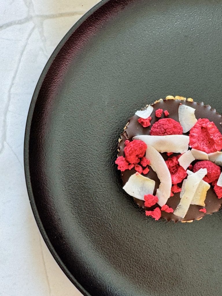 Prim-plan cu desert fara coacere din quinoa expandata si ciocolata, decorat cu zmeura liofilizata si fulgi de cocos