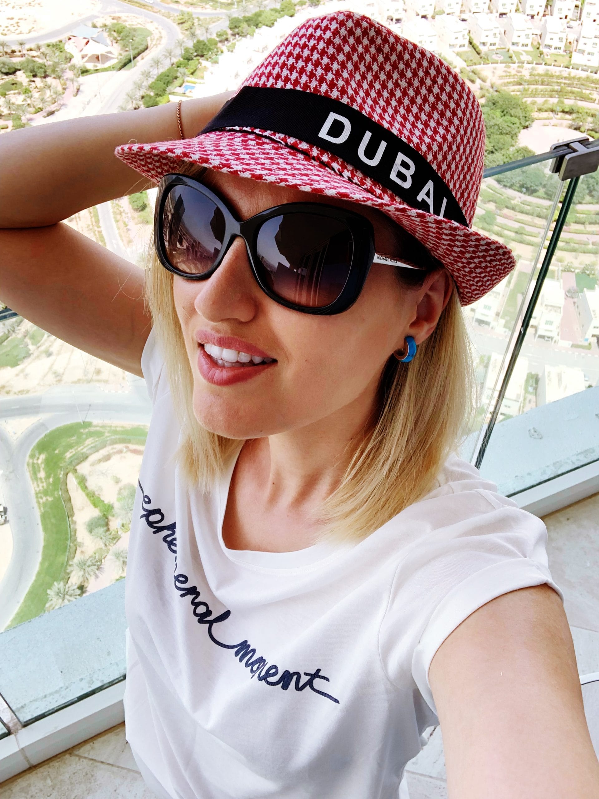 Selfie pe balconul camerei de hotel din Dubai cu o palarie pe care scrie Dubai