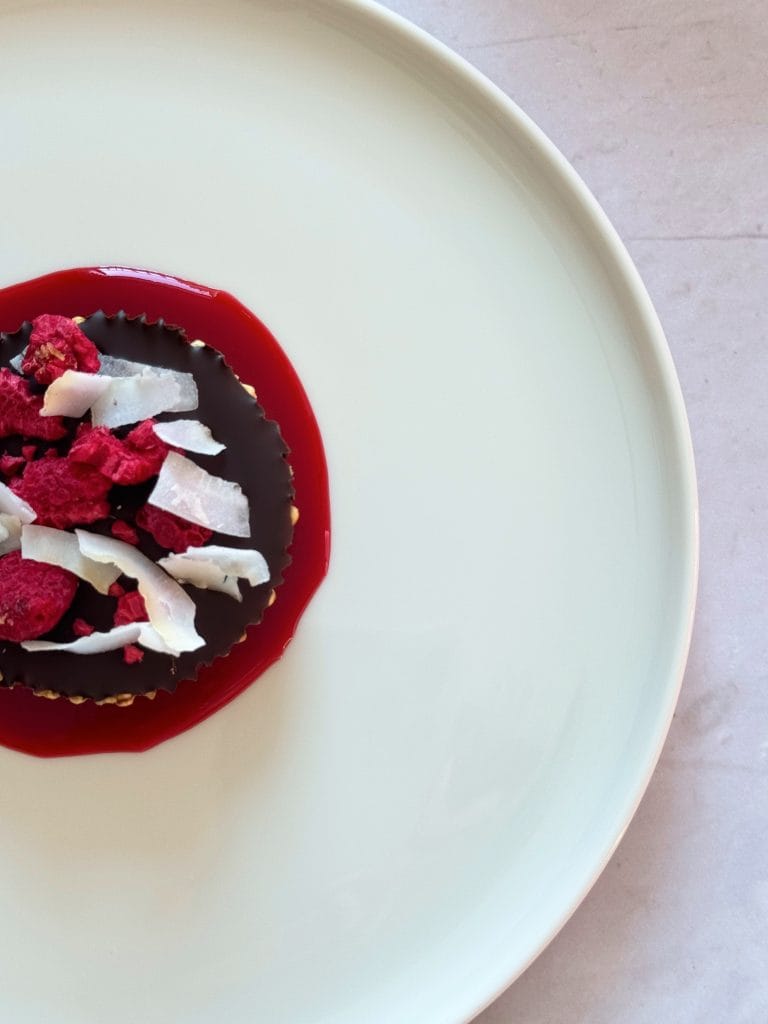 Desert fara coacere cu quinoa expandata si ciocolata, servit cu coulis de zmeura, zmeura liofilizata si fulgi de cocos