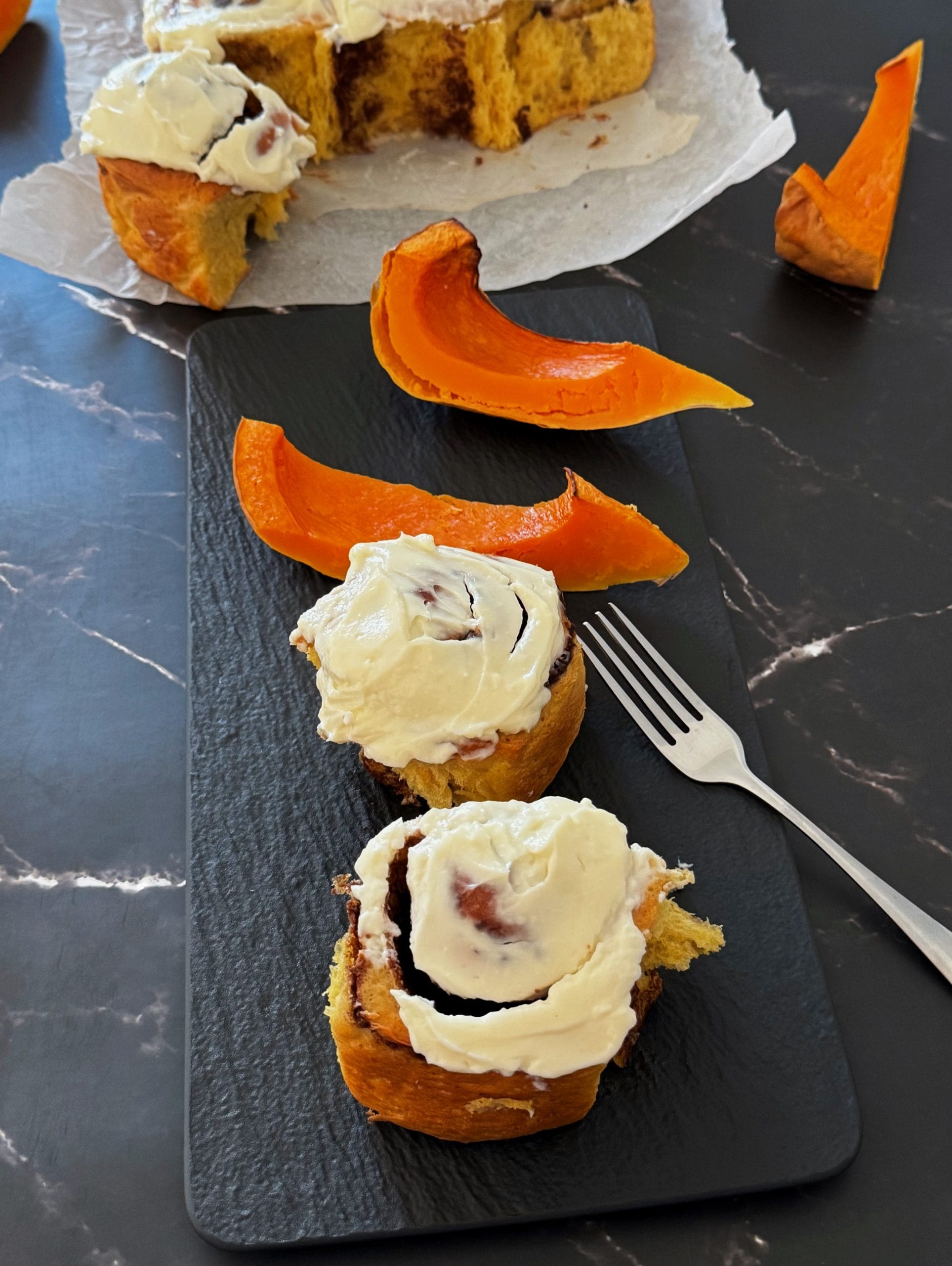 Pumpkin cinnamon rolls with cream cheese frosting, served with slices of roasted pumpkin