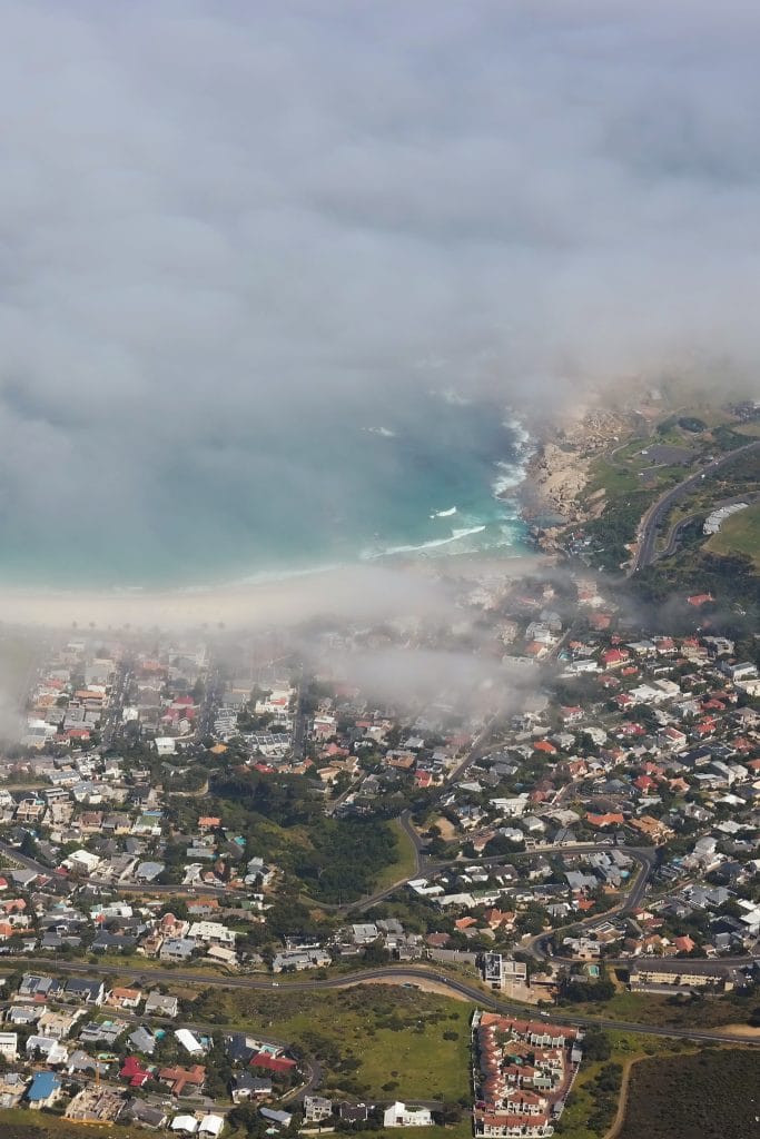 O perspectiva de sus de pe Table Mountain surprinzand zona urbana si coasta partial acoperite de un strat dens de nori de tip patura.