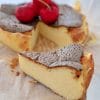 Prim-plan cu o felie cremoasă de cheesecake ars în stil basc, cu crustă caramelizată și cireșe roșii în fundal