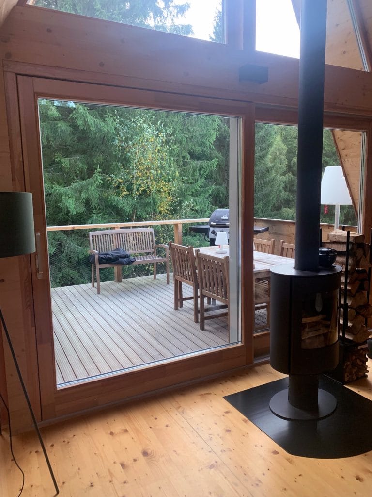 Interior de living cu șemineu modern, lemn de foc și uși glisante spre terasa cu masă și pădure de brazi, la Străjerii Verzi, Șirnea