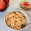Chicken and carrot salad with Greek yogurt in a white bowl, with tomatoes, bell pepper and cucumbers in the background