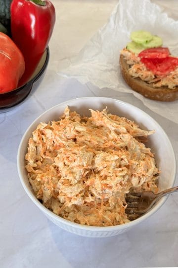 Chicken and carrot salad with Greek yogurt in a white bowl, with tomatoes, bell pepper and cucumbers in the background
