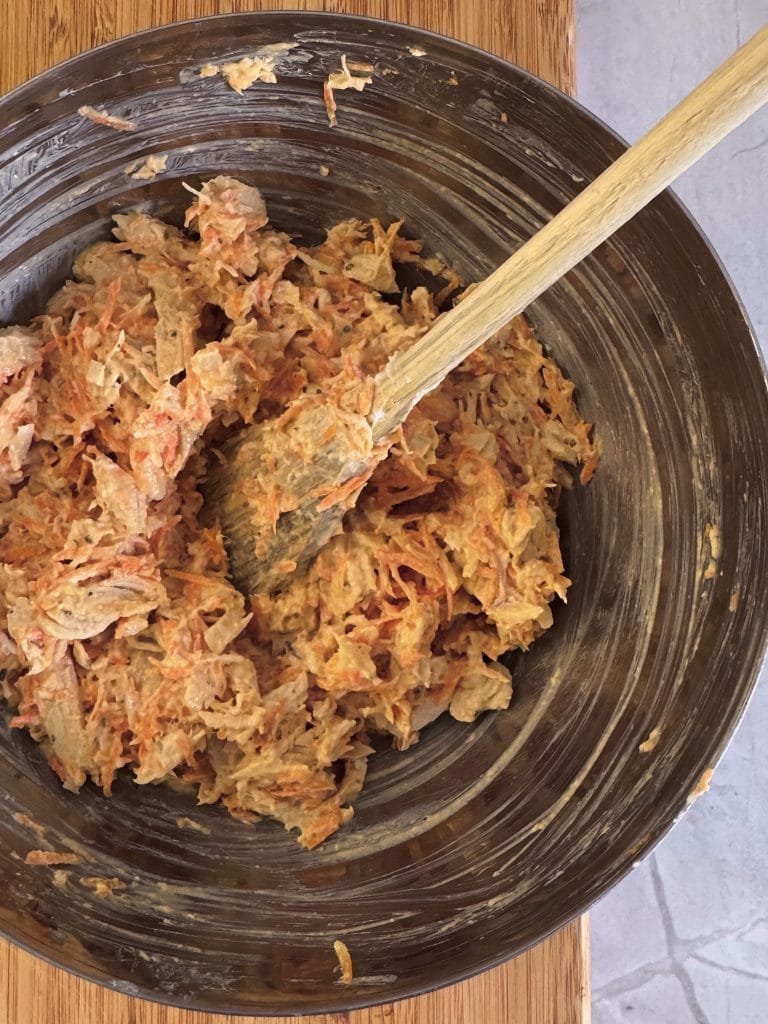 Chicken and carrot salad with Greek yogurt being stirred with a wooden spoon in a steel bowl