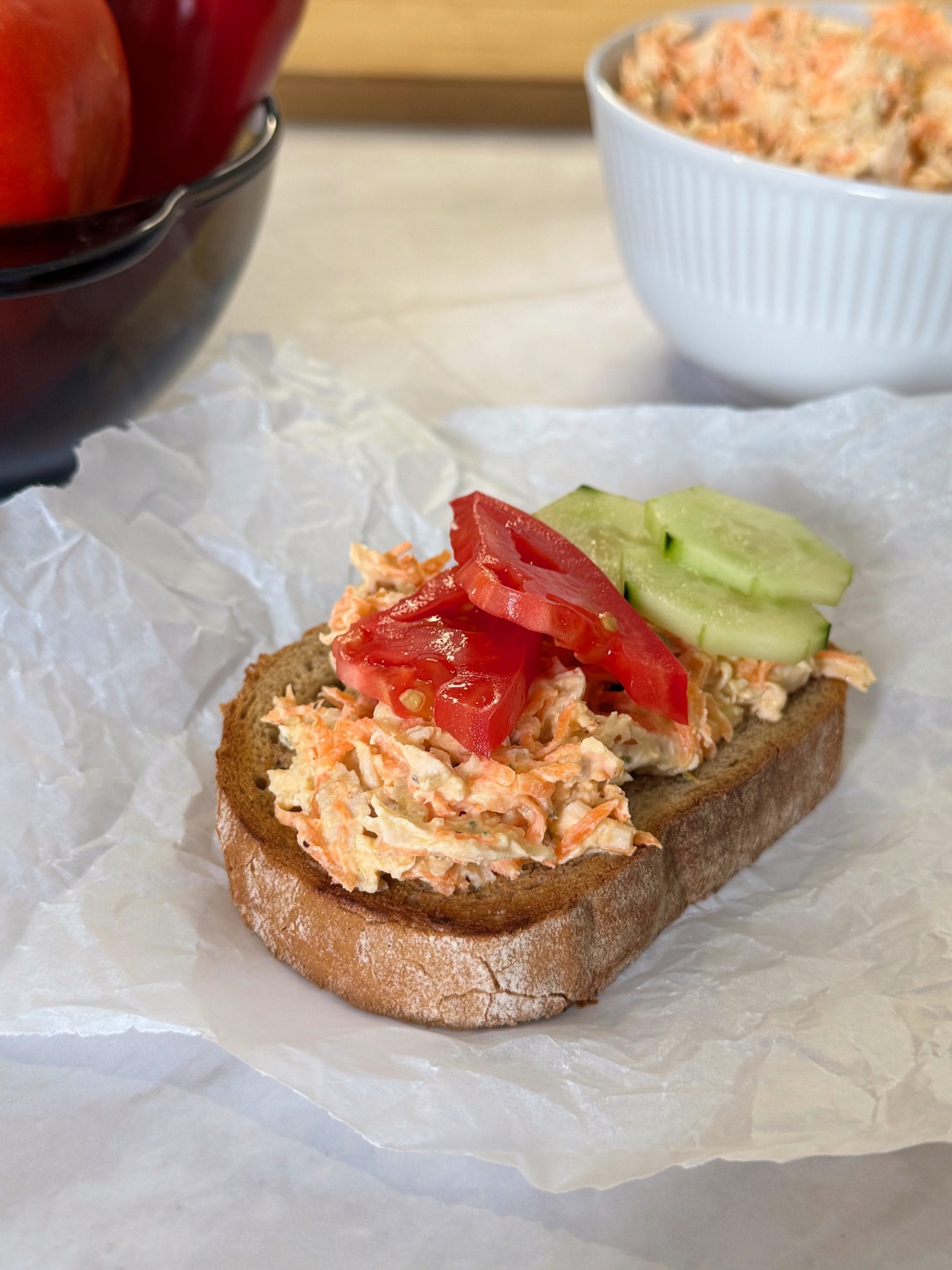 Toasted bread slice topped with chicken and carrot salad, garnished with tomato and cucumber slices