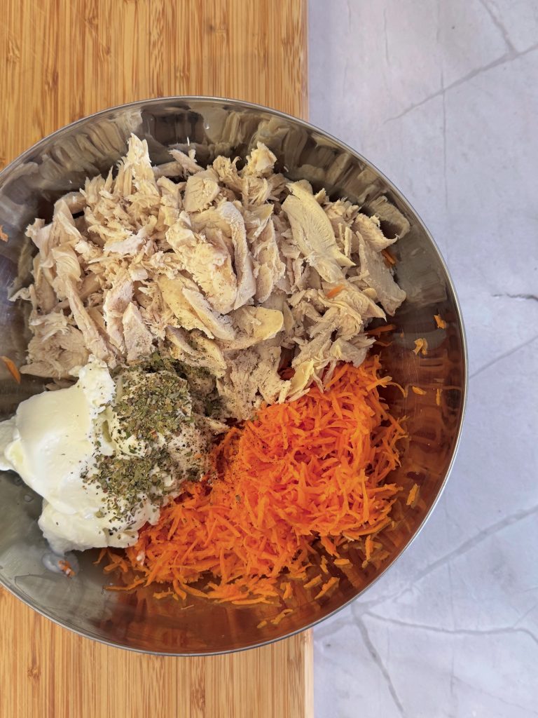 Cooked shredded chicken breast, grated carrot, Greek yogurt and seasonings arranged in a bowl before mixing