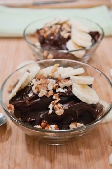 Bowls of chocolate peanut butter pudding topped with banana slices and chopped walnuts