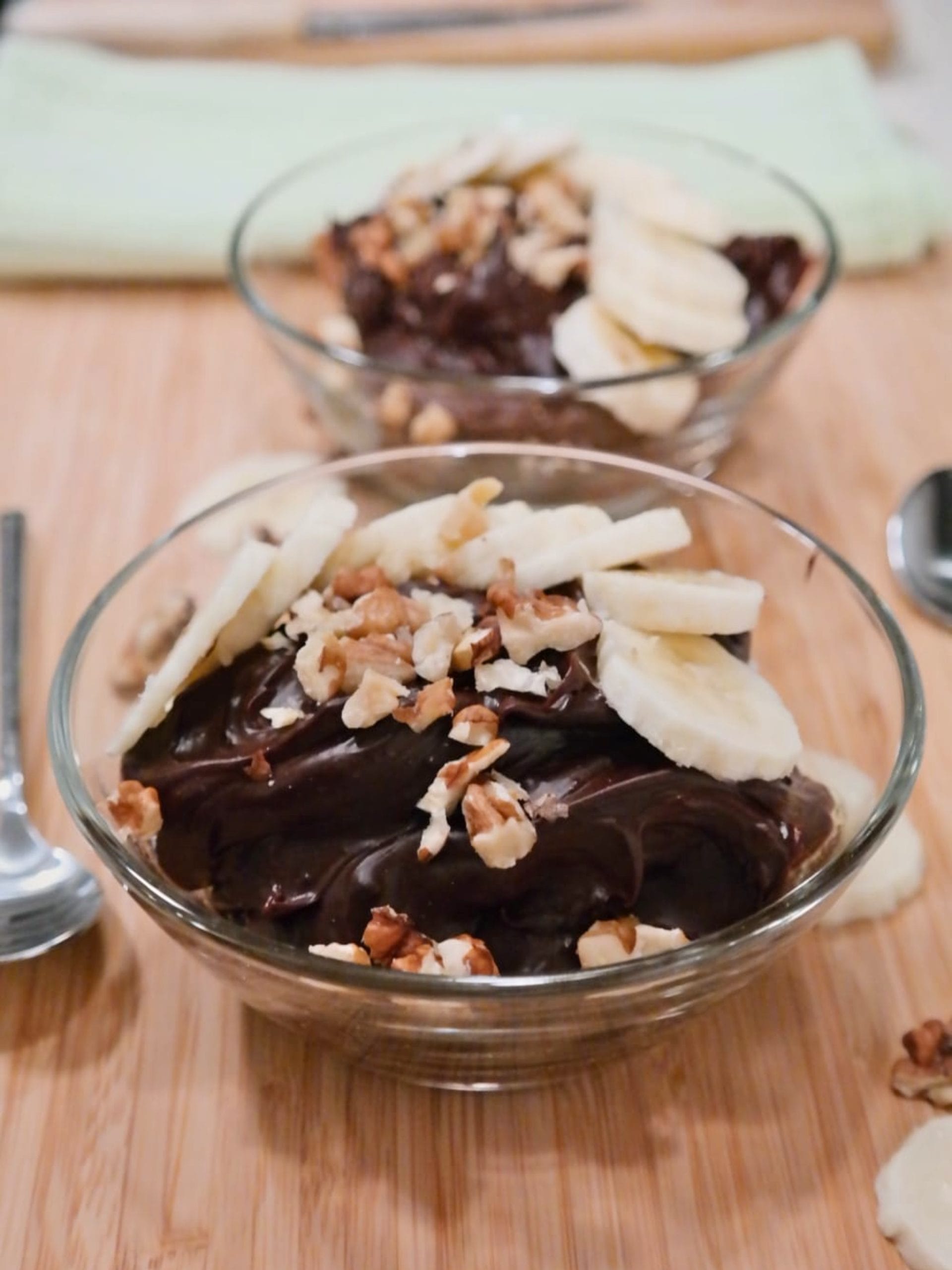 Bowls of chocolate peanut butter pudding topped with banana slices and chopped walnuts