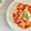 Bol cu gnocchi în sos de roșii, presărat cu fulgi de parmezan și frunze de busuioc proaspăt, pe un blat de marmură