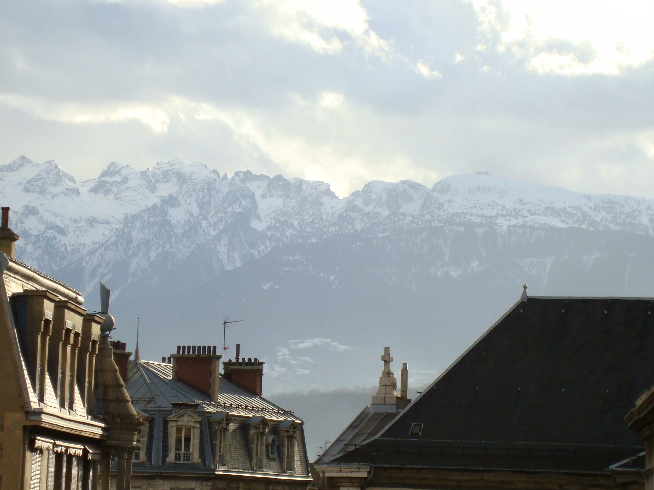 Munții Alpi acoperiți de zăpadă, ridicându-se deasupra acoperișurilor tradiționale franțuzești din Grenoble