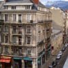 Street in central Grenoble lined with elegant French buildings, with snow-capped mountains on the horizon