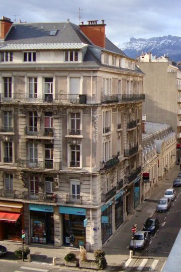 Stradă din centrul Grenoble, cu clădiri elegante franțuzești și munții înzăpeziți la orizont