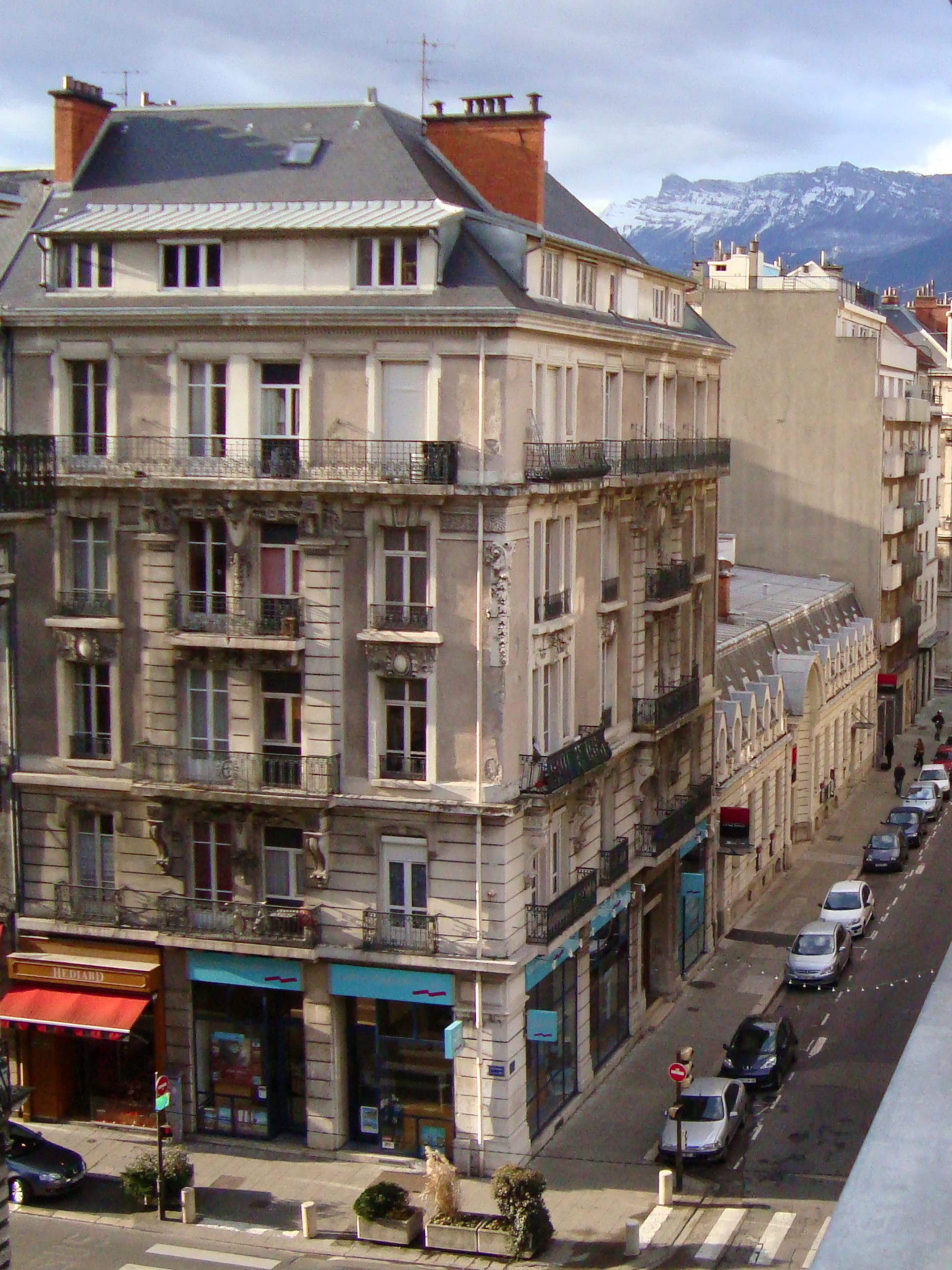 Stradă din centrul Grenoble, cu clădiri elegante franțuzești și munții înzăpeziți la orizont