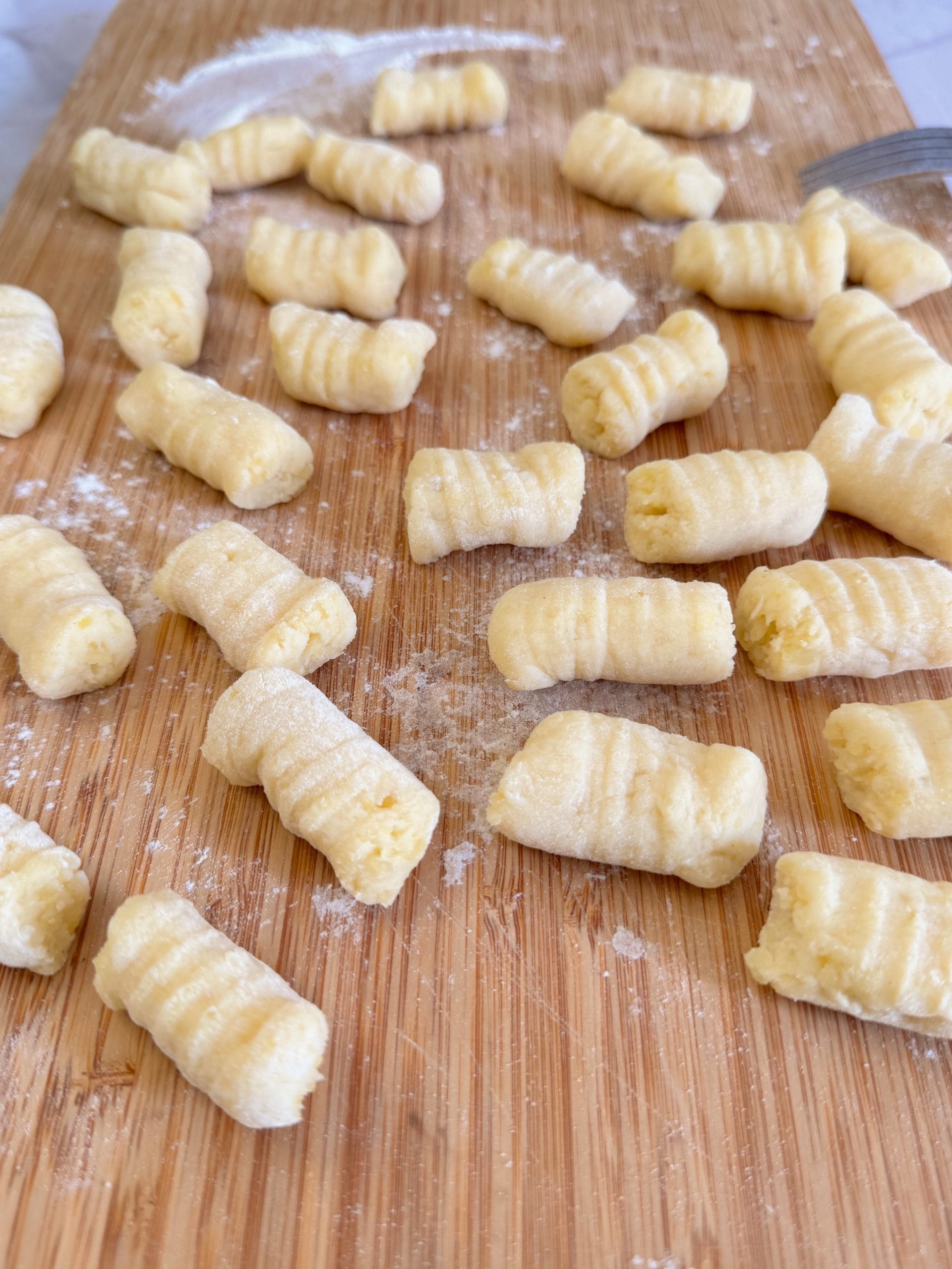 Gnocchi crude, făcuți în casă, așezați pe un blat de lemn presărat cu făină, cu striații tradiționale de furculiță