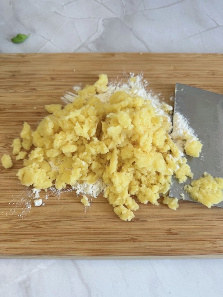 Cartofi fierți și pasați, amestecați cu făină pe un blat de lemn, alături de un cuțit de patiserie, pregătiți pentru aluatul de gnocchi