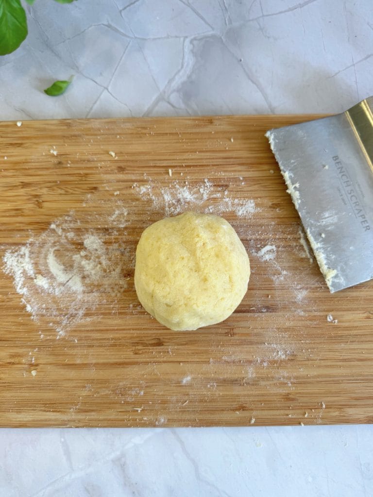 Bilă de aluat de cartofi pentru gnocchi, așezată pe un blat de lemn presărat cu făină, alături de un cuțit de patiserie