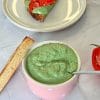 Spinach ricotta cream in a pink bowl, next to a slice of toast topped with the cream and sliced tomatoes