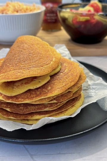 Teanc de lipii proteice rumenite pe hârtie de copt, pe o farfurie neagră, una îndoită deasupra, cu salata de pui cu morcov, chutney de mango și o salată de legume în fundal